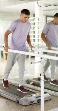 Vertical video: Man in rehabilitation walking on treadmill using parallel bars for support