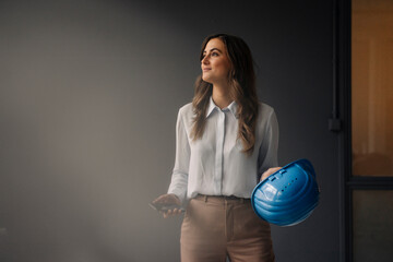 Smiling young businesswoman holding hard hat and cell phone