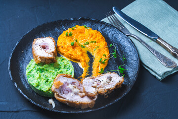 Chicken Cordon Bleu with carrot puree and mashed potatoes with spinach on a black mica board. A traditional French dish in an original presentation. Healthy eating and diet concept.