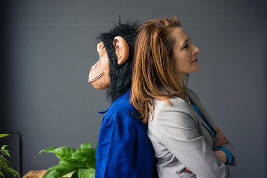 Businesswoman standing face to face with a trainee, wearing monkey mask and blue oevrall