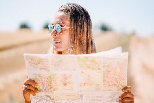 Blond young woman wearing mirrored sunglasses holding map looking at distance