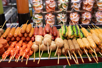 A food stall at a night market on Walking Street, featuring a pile of sausages and meatballs on wooden skewers.