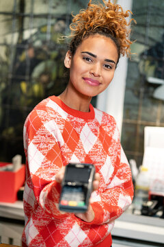 Young woman working in fashion store, holding card reader