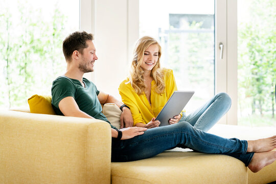 Couple sitting on couch in their new home, using digital tablet