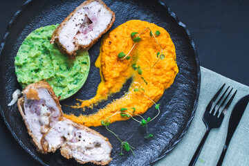 Chicken Cordon Bleu with carrot puree and spinach mashed potatoes on a black board top view. A traditional French dish in an original presentation. Healthy eating and diet concept.