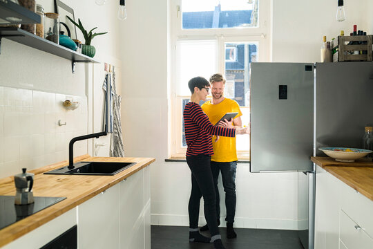 Happy couple with tablet in front of their fridge doing online shopping for groceries - Powered by Adobe