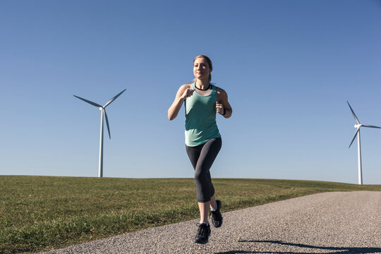 Young woman jogging on field way, wind wheels in the background