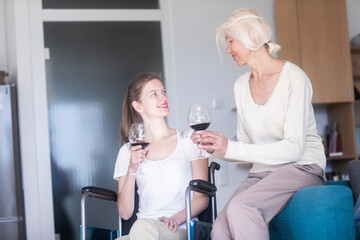 Mother and daughter in the wheelchair with a glass of red wine at home