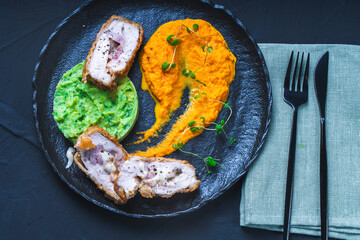 Chicken Cordon Bleu with carrot puree and spinach mashed potatoes on a black board top view. A traditional French dish in an original presentation. Healthy eating and diet concept.
