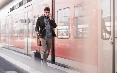 Young man on cell phone walking on station platform along commuter train