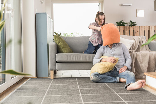 Young man and little girl having a pillow fight in the living room
