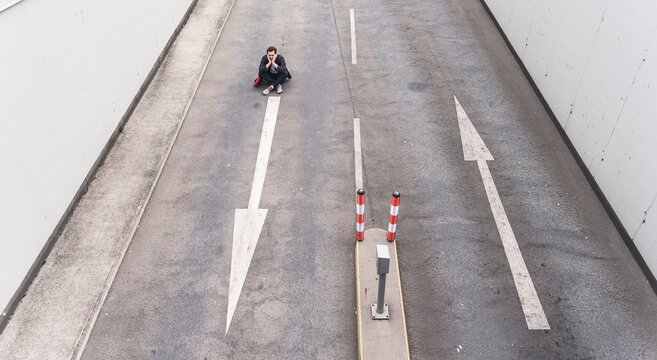 Businessman sitting on road with arrow signs