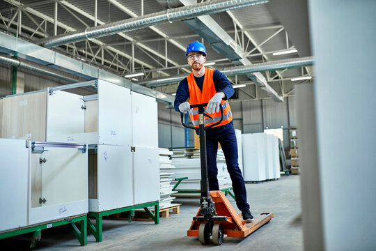 Worker riding on pallet jack in factory