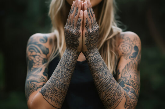 Caucasian tattooed woman joining hands in a meditative pose, showing traditional sak yant tattoos