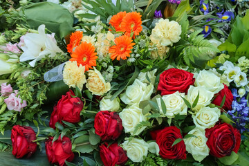 Several memorial flower bouquets at the grave in June. Colorful funeral flowers at the cemetery in summer. Red and white roses. Orange Gerberas and yellowish carnations. 