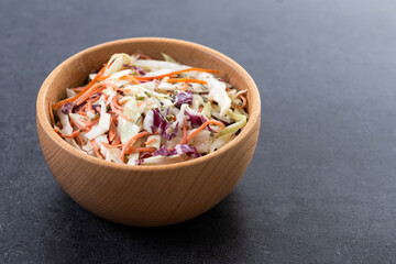 Coleslaw salad in wooden bowl on black slate background. Copy space