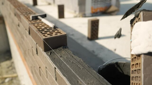 Skilled bricklayer spreading cement methodically while constructing sturdy residential brick wall using professional masonry techniques