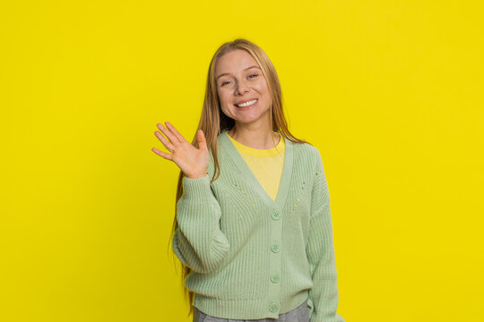 Young Caucasian woman smiling friendly at camera, waving hands gesturing hello greeting or goodbye welcoming with invitation hospitable expression. Pretty girl isolated on yellow studio background