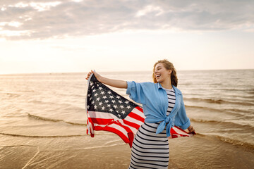 Young woman holding national American flag walking ocean beach.  4th of July. America Independence...