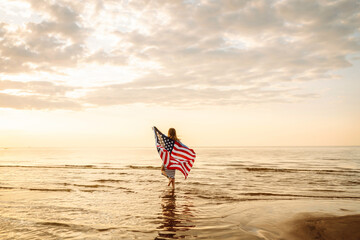 Young woman holding national American flag walking ocean beach. 4th of July. America Independence Day concept.