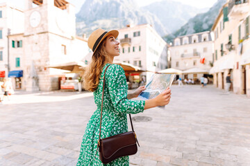 Adventurous woman navigating in with topographic map by city. Woman wanderer with trendy look searching direction on location map while traveling abroad in summer. Tourism.