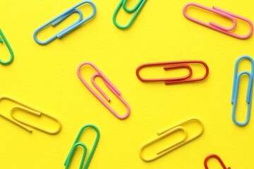 Colorful paper clips on yellow background, flat lay