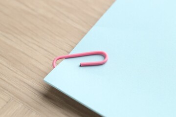 Paper note with clip on wooden table, closeup. Space for text