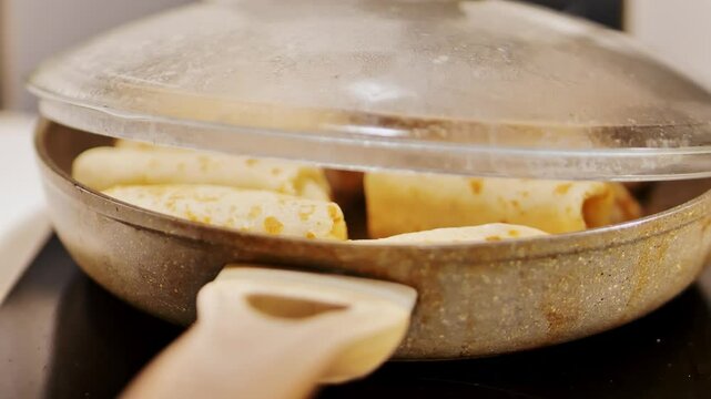 Traditional Russian blini cooking in pan with wooden handle and steamy glass lid