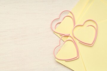 Heart shaped paper clips and notes on wooden table, top view. Space for text