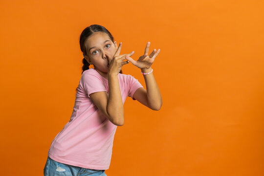 Cheerful funny bully young cute girl making faces at camera, fooling around, joking, aping with silly face, teasing. Preteen child kid 10 years old on orange background. Little children - Powered by Adobe