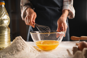 Close-up of bakers hands whisking eggs in a glass bowl, preparing ingredients for bread or pastry in an authentic home kitchen setting. Focus on the process and artisanal craftsmanship