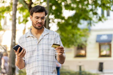 Angry Indian man trying to pay online shopping with smartphone blocked credit card. Annoyed young...