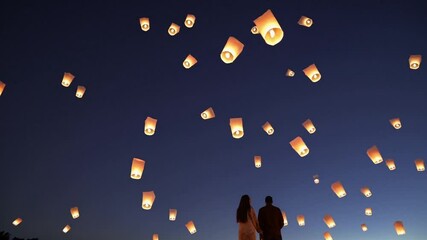 Night Sky Lantern Release: A romantic couple silhouetted against a breathtaking display of hundreds of glowing sky lanterns ascending into the night sky. A mesmerizing scene of hope, wishes.