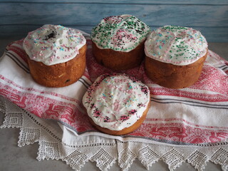 Four Classic Close up Rustic baking traditional Easter cakes orthodox Easter Lace embroidered towel. Cupcakes white icing, colored sprinkles on blue wood background. Romantic wedding national dessert