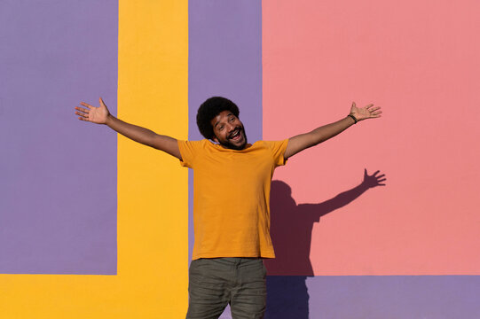 Cheerful man with arms outstretched standing against colored background