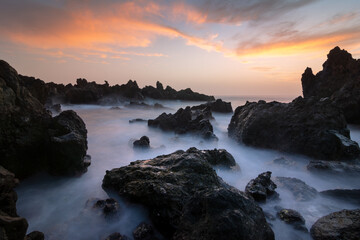 Scenic sunset view of rocky seashore with waves and misty water
