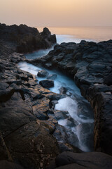 Scenic sunset view of rocky seashore with waves and misty water