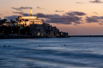 Fototapeta premium Twilight seascape view of the Tel-Aviv-Jaffa coastline and landmark St. Peter's Church illuminated in the early evening light.