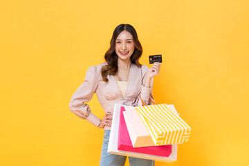 Beautiful Asian woman holding colorful shopping bags and credit card in studio isolated yellow...