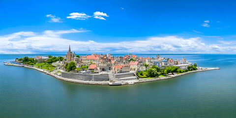Fototapeta premium Aerial view of an island town showcases buildings, greenery, and a serene blue sea under a bright sky perfectly.