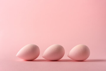 Soft makeup sponges in pastel pink tones on a minimal background