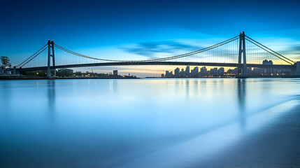 Obraz premium Suspension Bridge Spans Serene Waters at Dusk with City Skyline Beautifully Reflected