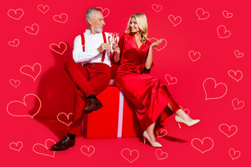 Full length photo of mature couple sitting gift box celebrate eve time noel drink champagne isolated over red color background