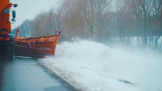 A snow plow truck clears snow from the road, side of road after a snowstorm and blizzard. Snowplow clears road of snow after a snowfall, salting street in winter time, snow removal. Road maintenance