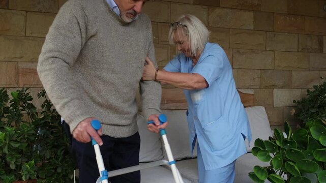 Nurse assisting elderly man using walker to sit down
