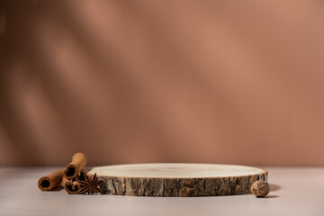 Wooden round podium product showcase on brown background with spices cinnamon, nutmeg and star anise. Aromatic perfumed cosmetic background