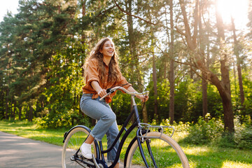 Happy woman riding bicycle bike on sidewalk in city green park outdoors. Active lifestyle concept.