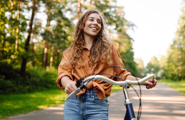 Happy woman riding bicycle bike on sidewalk in city green park outdoors. Active lifestyle concept.