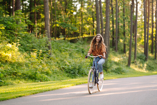 Happy woman riding bicycle bike on sidewalk in city green park outdoors. Active lifestyle concept.
