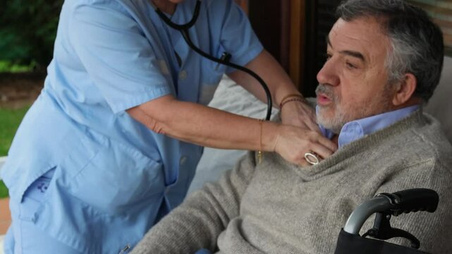 Nurse examining elderly man in wheelchair using stethoscope